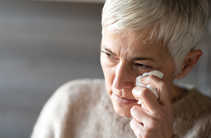Elderly woman wiping away tears from her eye and looking into the distance