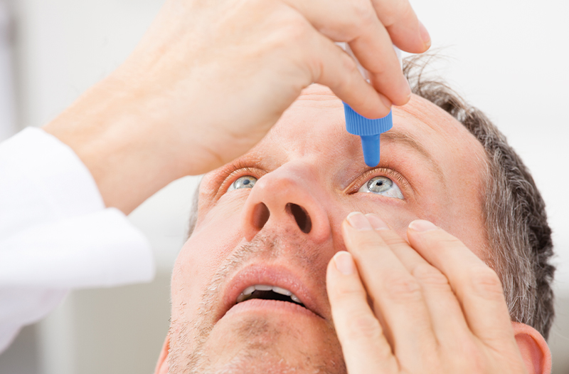 A person holding open one of their eyes whilst instilling eye drops