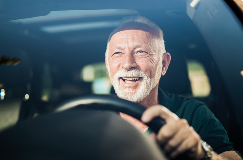 Happy elderly gentleman driving with the sun on his face