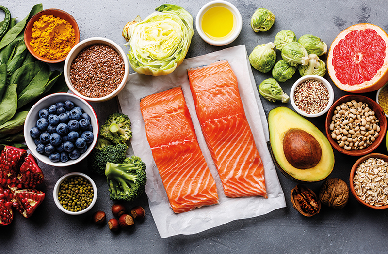 Two salmon fillets surrounded by a plethora of various fruits and vegetables
