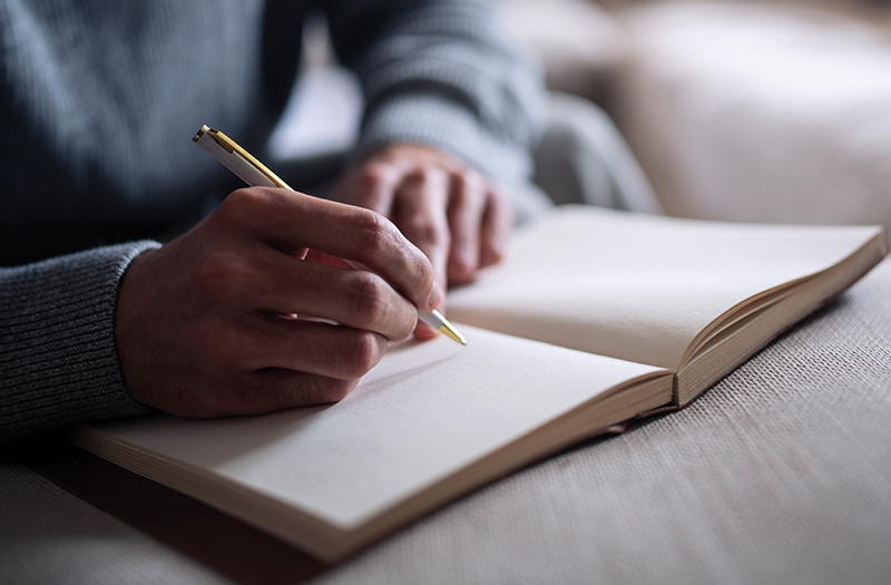A person writing in an empty notebook with a gold pen