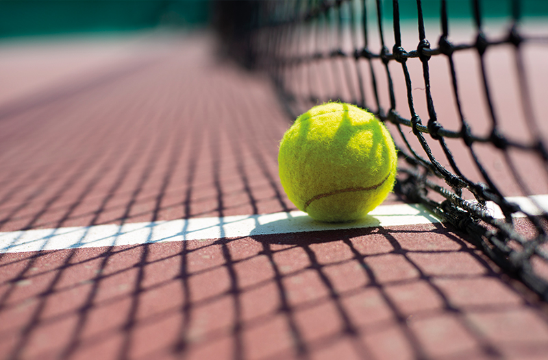 Tennis ball positioned in the shade of the net on the white line of a tennis court