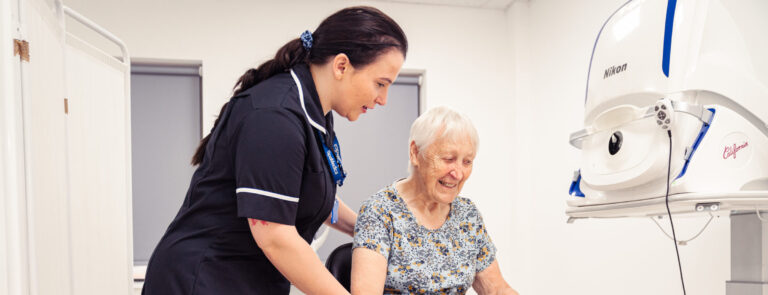 SpaMedica Health Care Technician helping a SpaMedica patient into her seat to carry out an eye exam