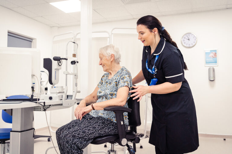 SpaMedica Health Care Technician helping a SpaMedica patient into her seat to carry out an eye exam