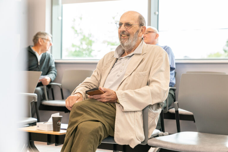 Happy SpaMecica patient sat in a waiting room holding his mobile phone in one hand