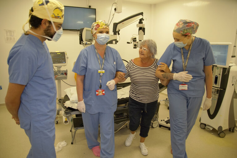 A smiling SpaMedica patient after surgery, being supported by SpaMedica nurses, with the surgeon looking on and smiling