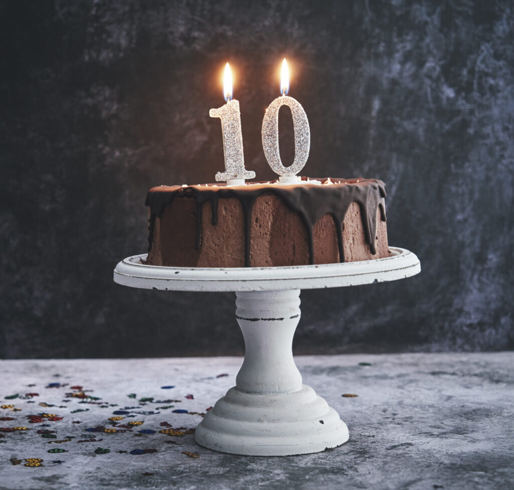 chocolate cake on a cake stand with lit candles resembling the number ten