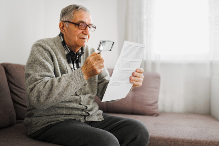 Senior man holding an magnifying glass he uses to help him read because he suffers from Wet Macular Degeneration.