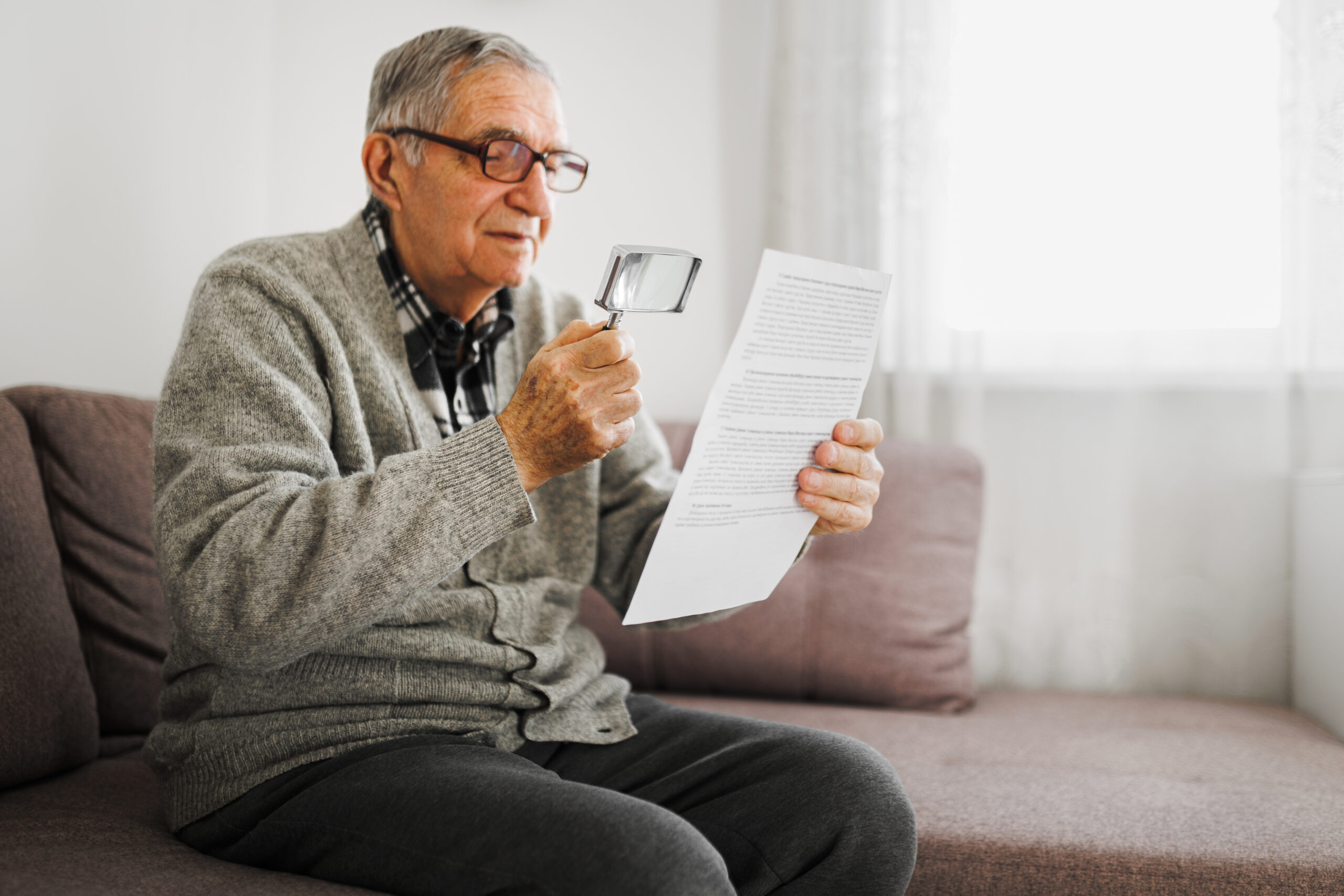 Senior man holding an magnifying glass he uses to help him read because he suffers from Wet Macular Degeneration.