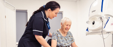 SpaMedica Health Care Technician helping a SpaMedica patient into her seat to carry out an eye exam