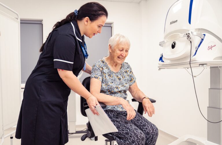 SpaMedica Health Care Technician helping a SpaMedica patient into her seat to carry out an eye exam