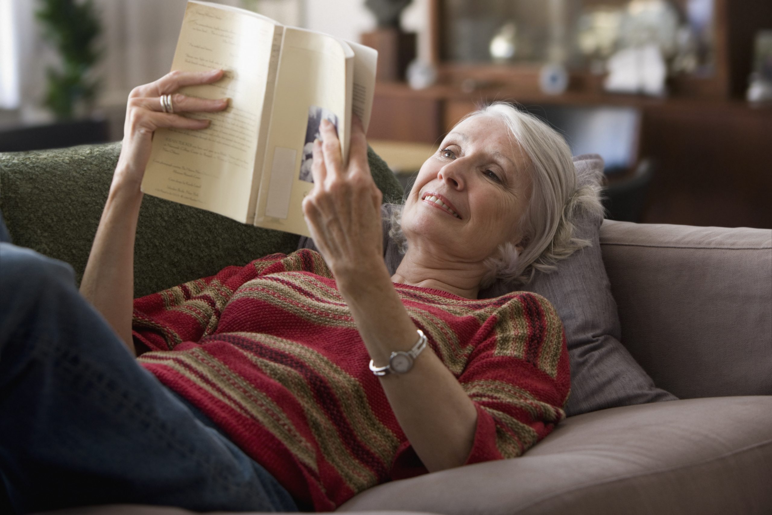 Elderly woman reading book on sofa