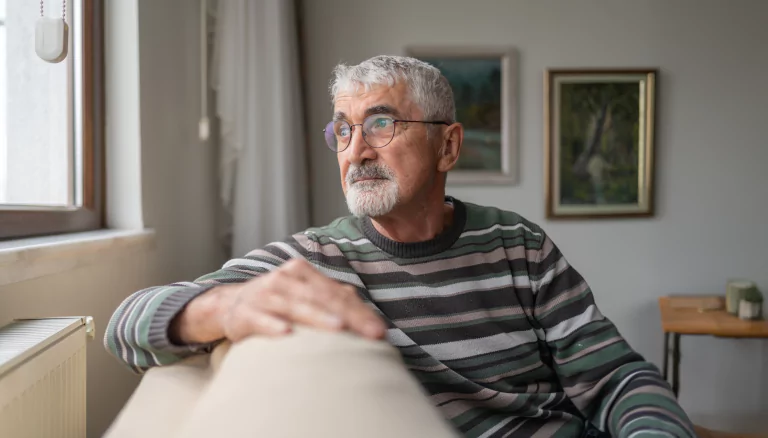 Elderly male looking out of window in deep thought